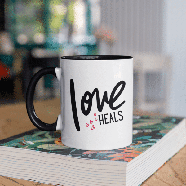 Love Heals black and white mug resting on a book in a cafe